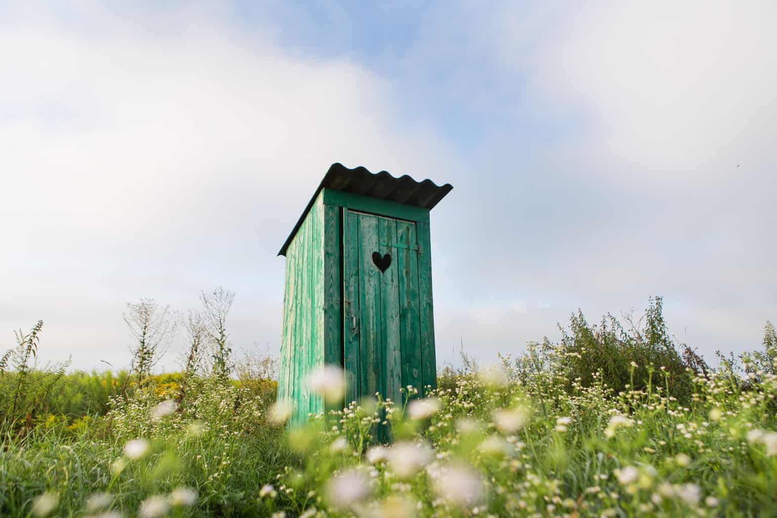 Blogbeitrag Campingtoiletten ohne Chemie Beitragsbild - Hölzernes Toilettenhäuschen auf der Wiese stehend